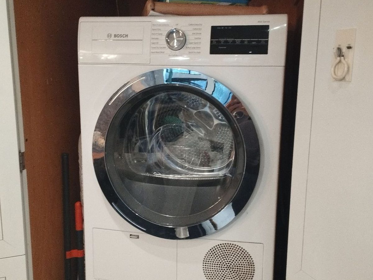 Bosch dryer stacked above a washer in a wooden closet