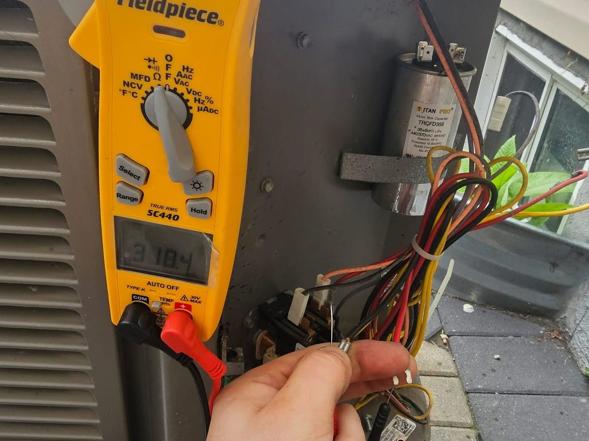 Tech diagnosing an AC unit with a Fieldpiece meter inside the electrical panel