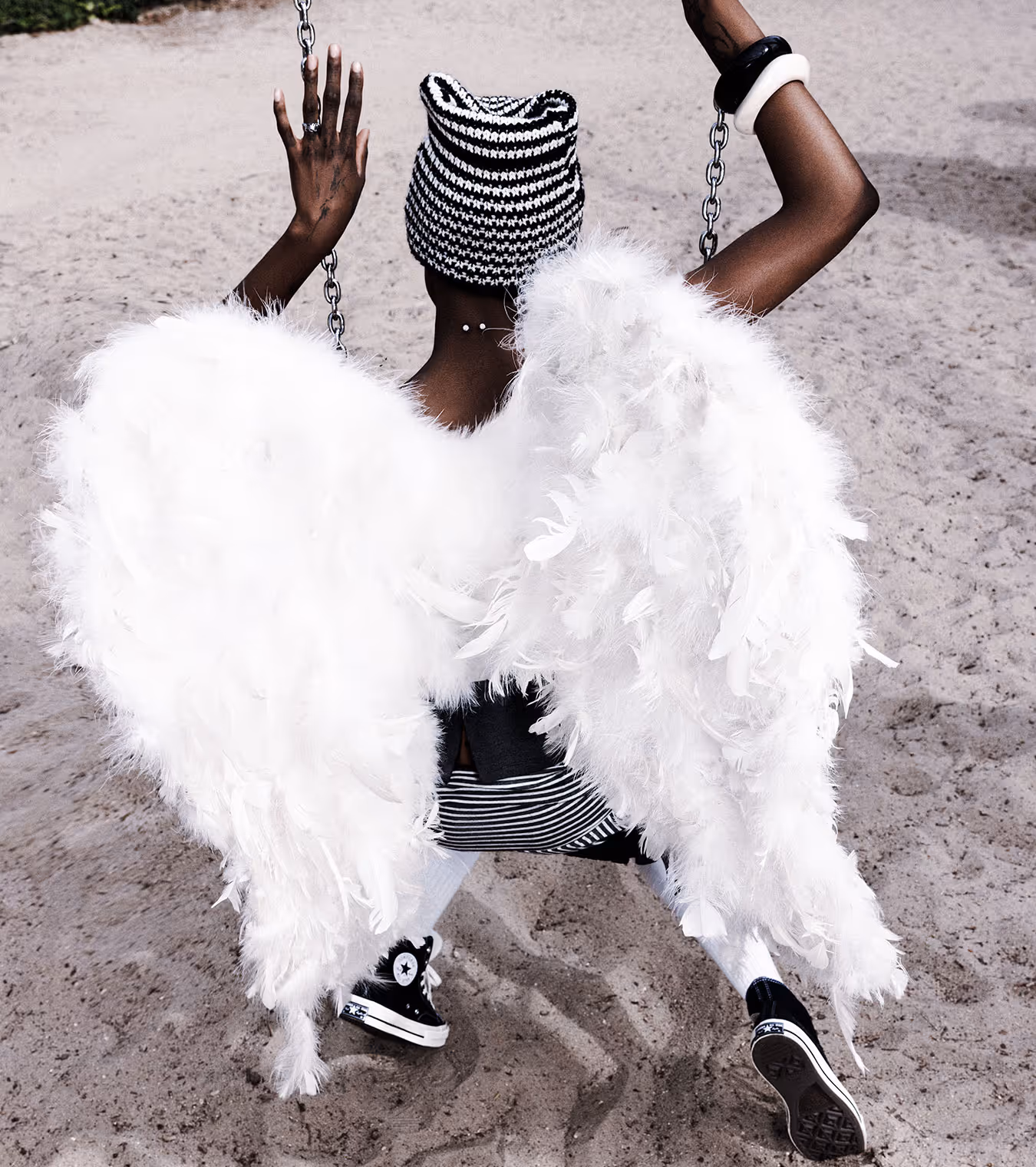 A black girl with angel wings on a swing from the back wearing CONVERSE.