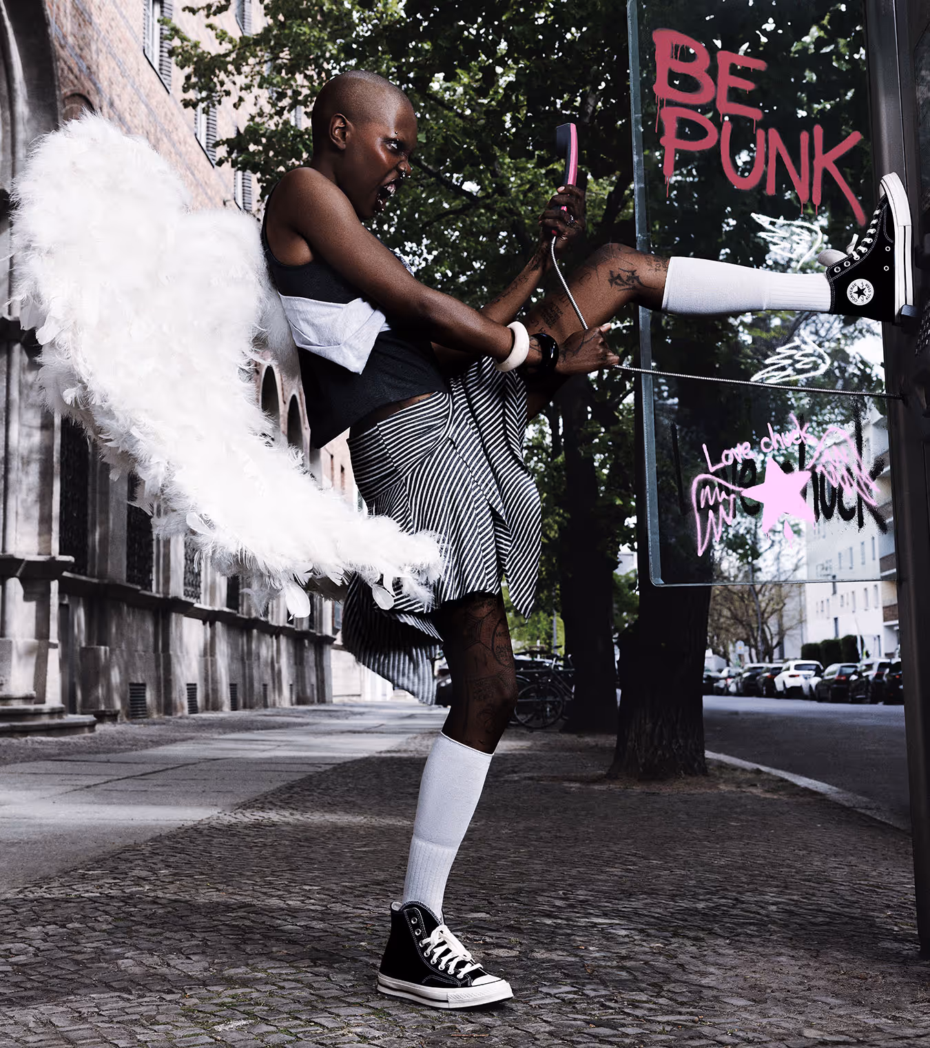 A black girl with angel wings at the phone booth wearing CONVERSE.