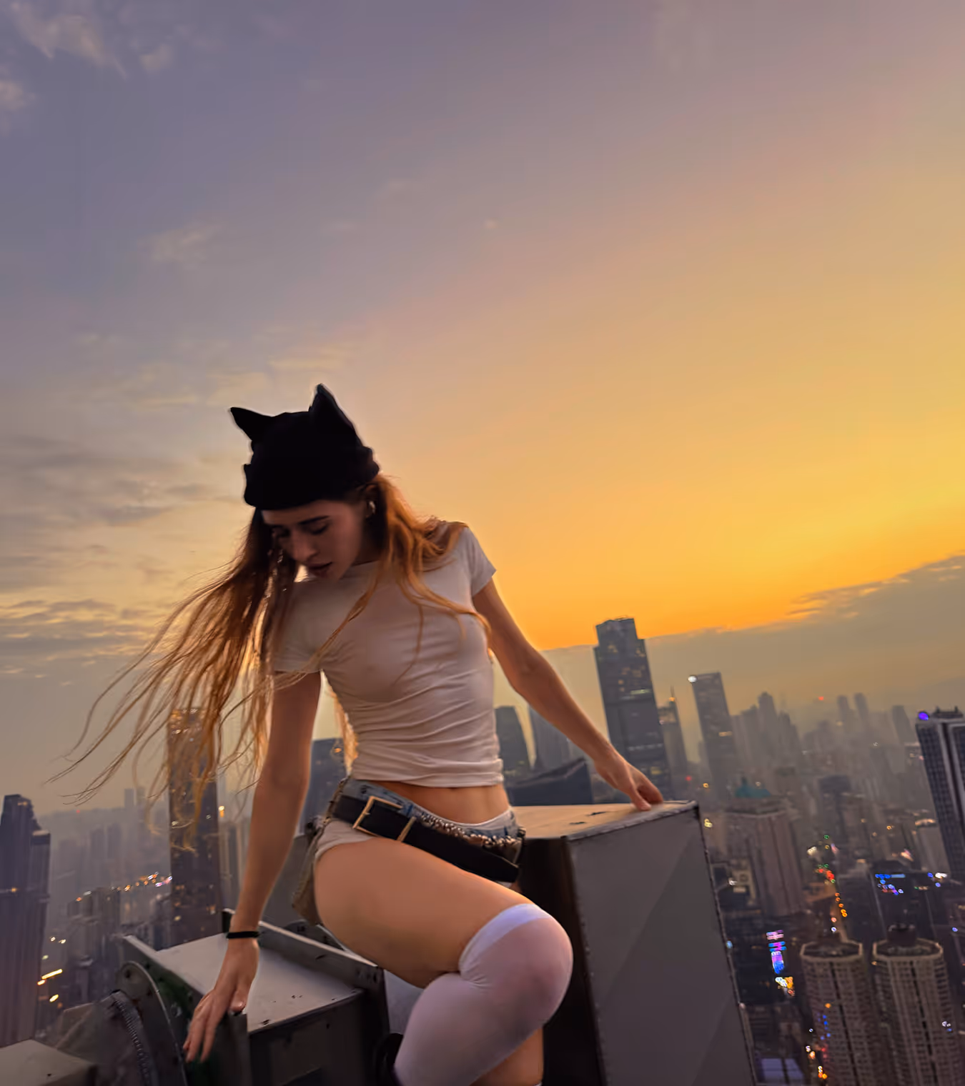 A woman at the edge of a building in stylish outfit at dusk.
