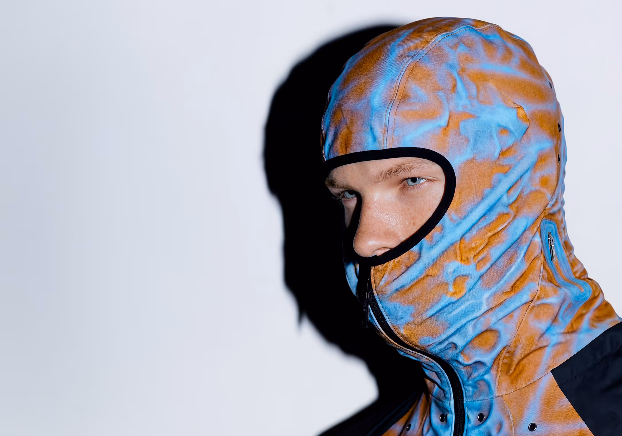 A man with blue eyes wearing a hooded tech jacket.