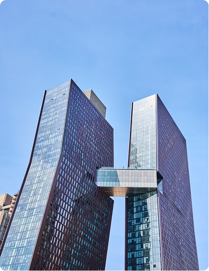 Two modern glass skyscrapers with a glass bridge connecting them against a clear blue sky.