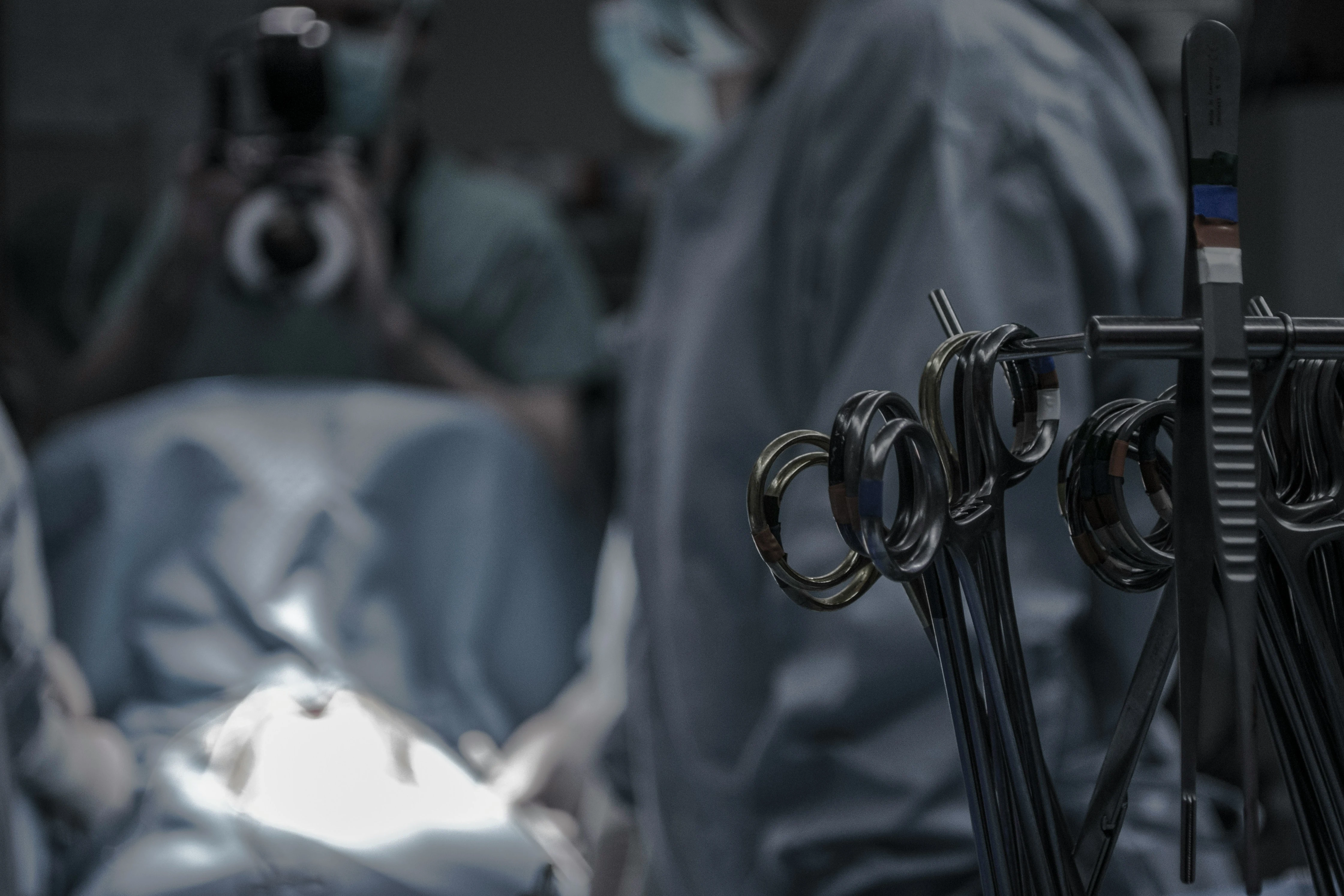Close-up of surgical scissors in focus with a blurred surgical team operating in the background.