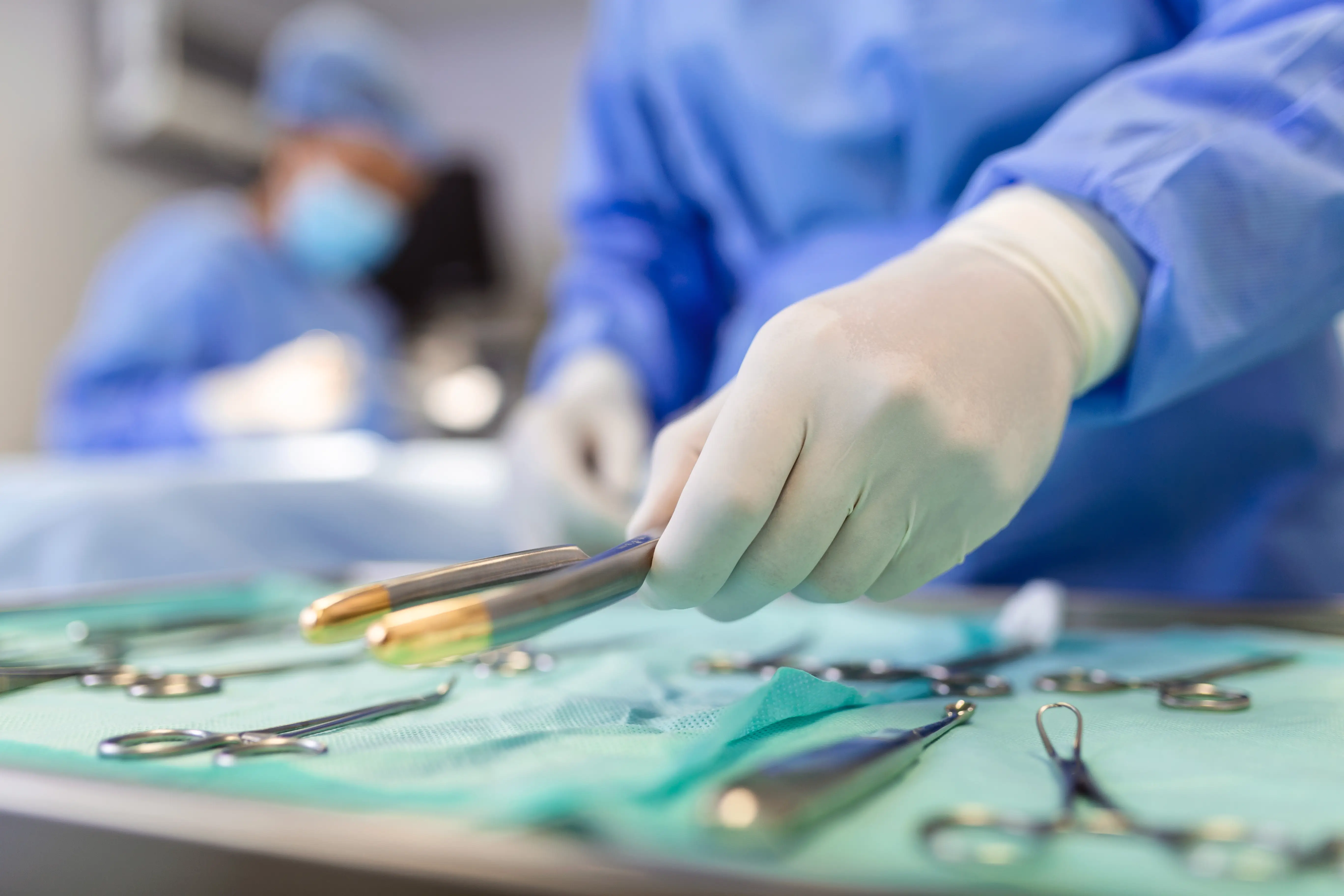 Gloved hand selecting a surgical tool from a sterile tray in an operating room.