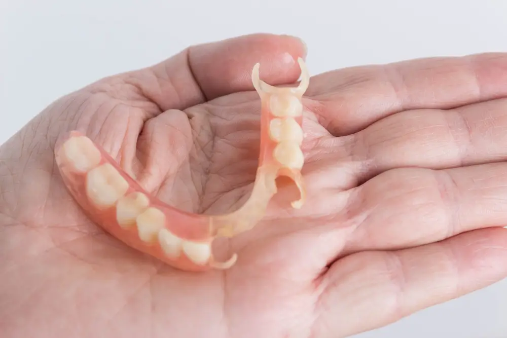 How do partial dentures look? See a hand holding a flexible removable partial denture.