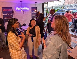 Three women engaged in conversation inside a modern event space with neon sign reading 'Fun Profiling' on the wall.
