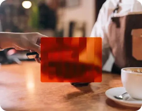A person holding a black card facing a barista over a wooden counter with a cup of coffee in the foreground.