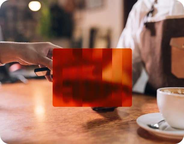 A person holding a black card facing a barista over a wooden counter with a cup of coffee in the foreground.