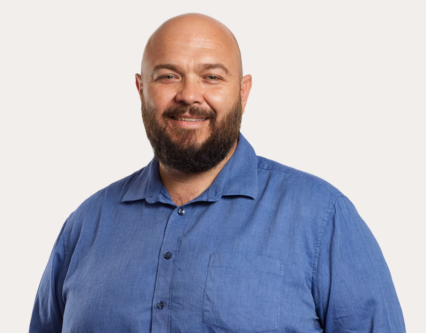 Smiling bald man with a beard wearing a blue button-up shirt against a plain light background.