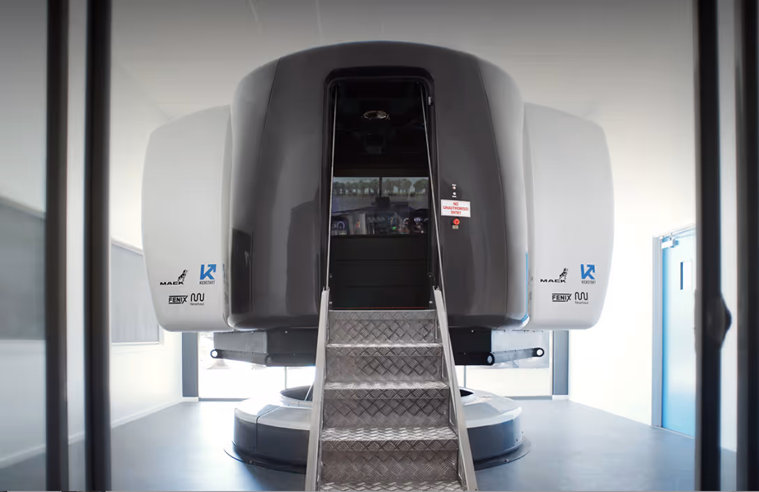 Flight simulator cockpit with metal stairs leading up to the open entrance inside a bright room.