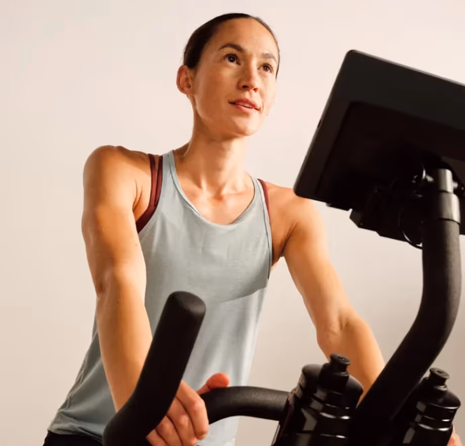 Woman wearing a tank top working out on a stationary exercise bike with a digital display.