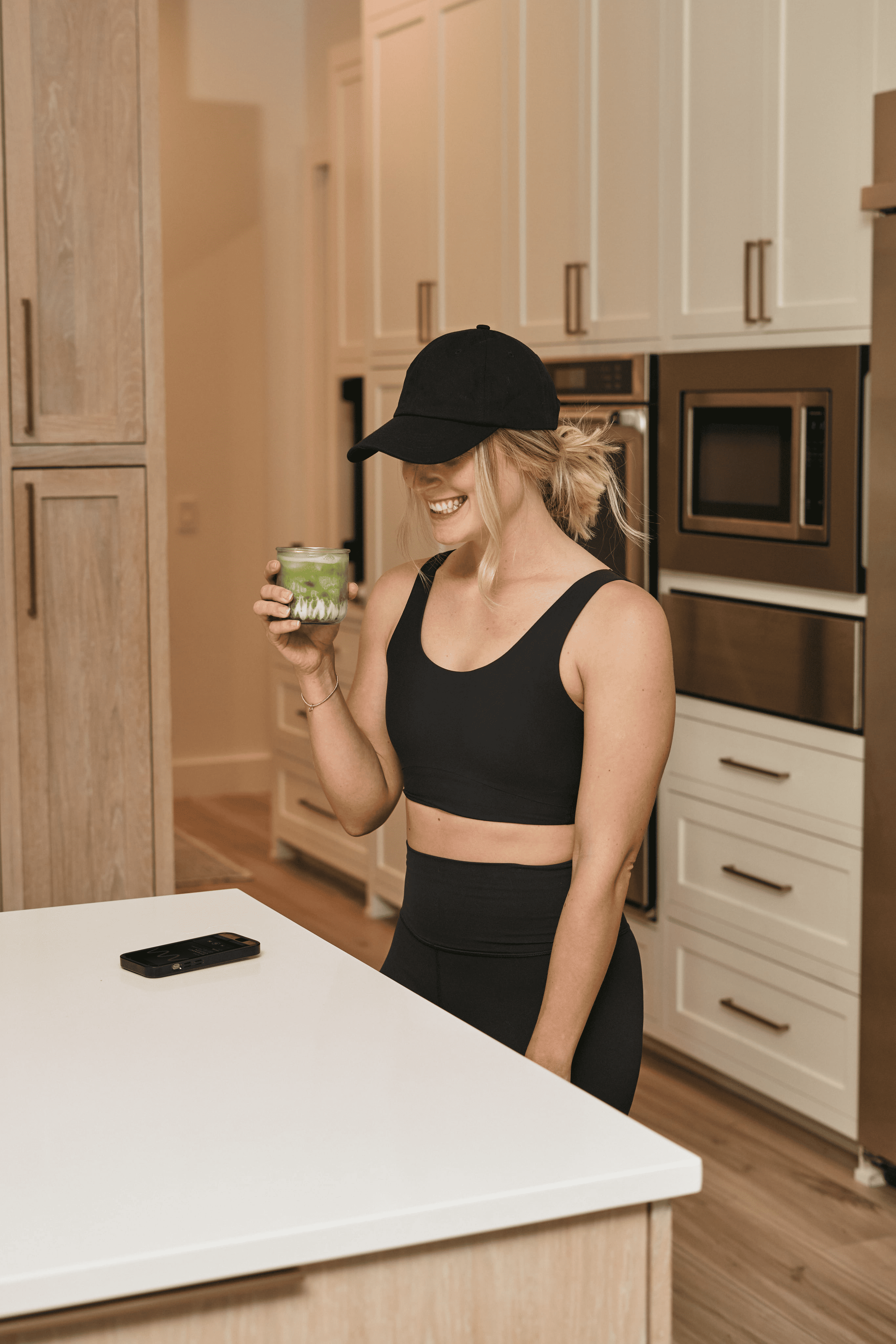 Individual in a kitchen holding a green smoothie, with a phone on the counter showing a sound frequency playback screen.