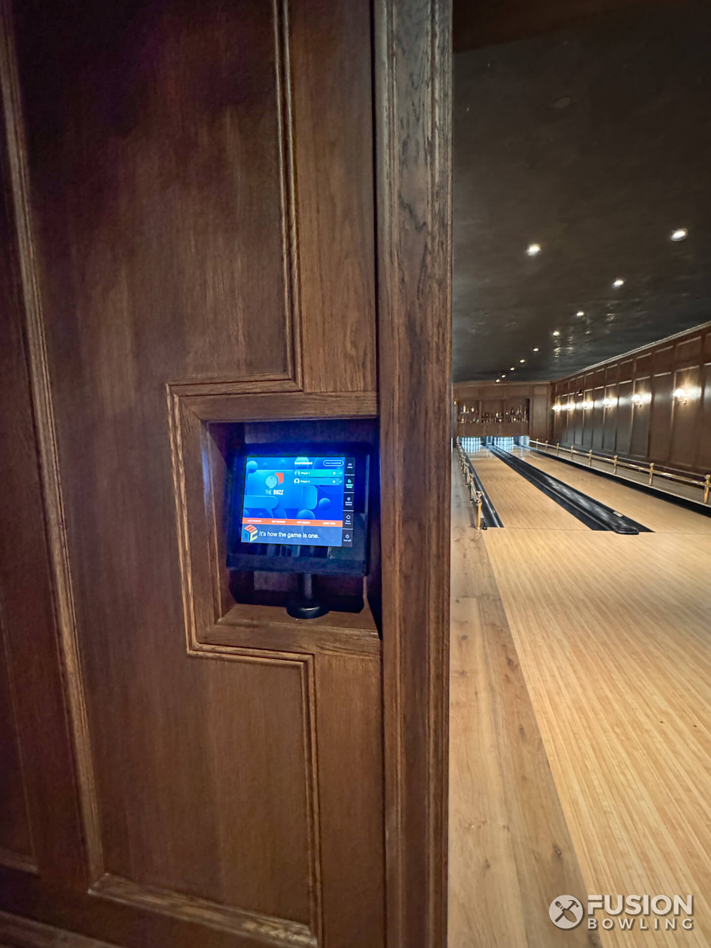 Bowling alley touch screen control mounted inside a custom wood panel wall niche.