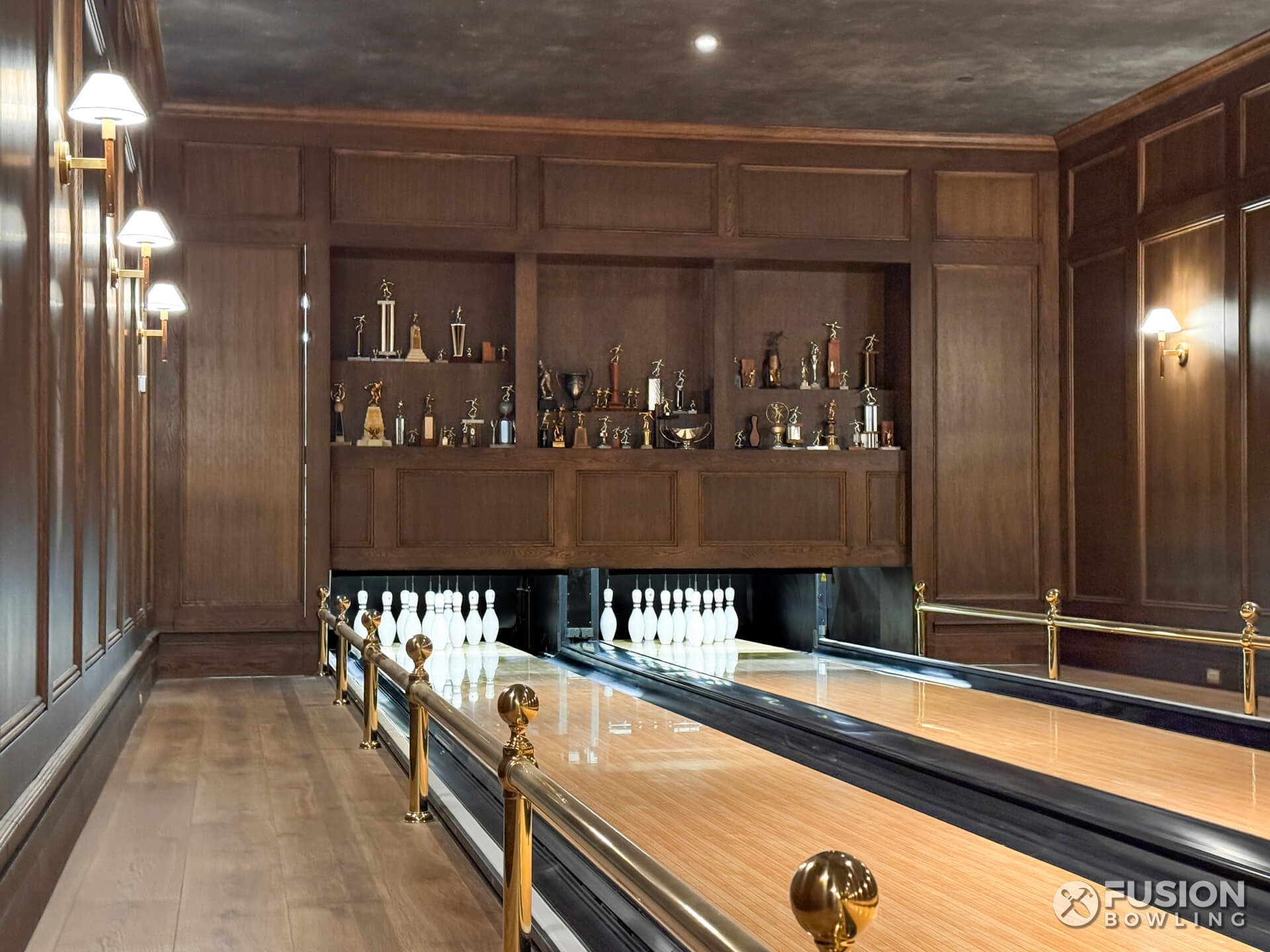 Custom home bowling alley with brass railings and trophy case over the bowling pins.