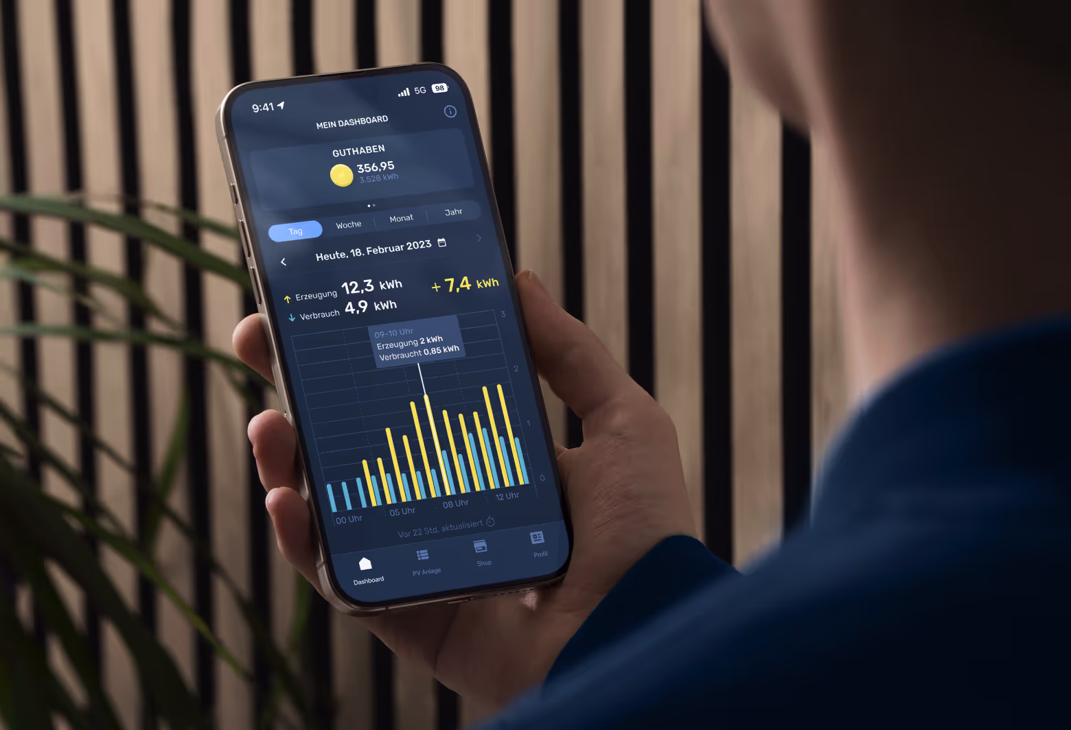Mann in blauem Pullover hält iPhone in der Hand mit EnerCloud App Screen vor Holzhintergrund