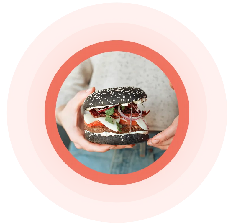 Person mit einem Gourmet-Burger mit schwarzem Sesambrötchen, Salat, Tomate, Zwiebel und Sauce.