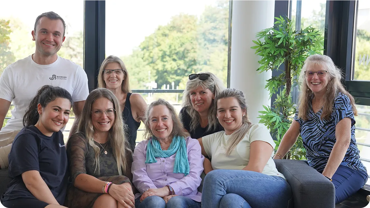 Ältere Frau, die mit blauen Hanteln trainiert, während sie auf einem grauen Gymnastikball im Wohnzimmer sitzt.