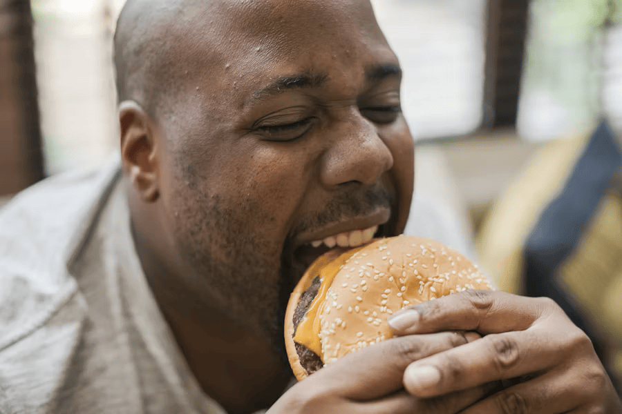 Übergewichtiger mann isst wegen einer Heißhunger attacke Fast Food.