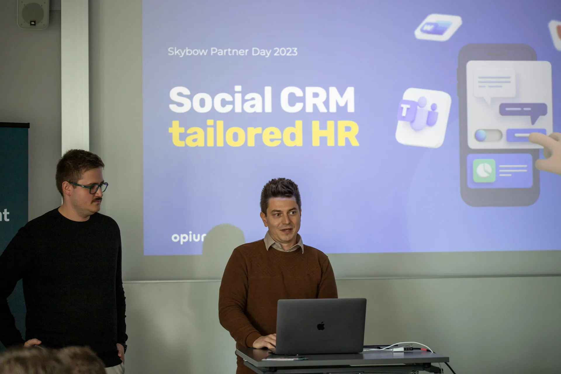 Two men presenting in front of a projected slide that reads 'Social CRM tailored HR' during Skybow Partner Day 2023.