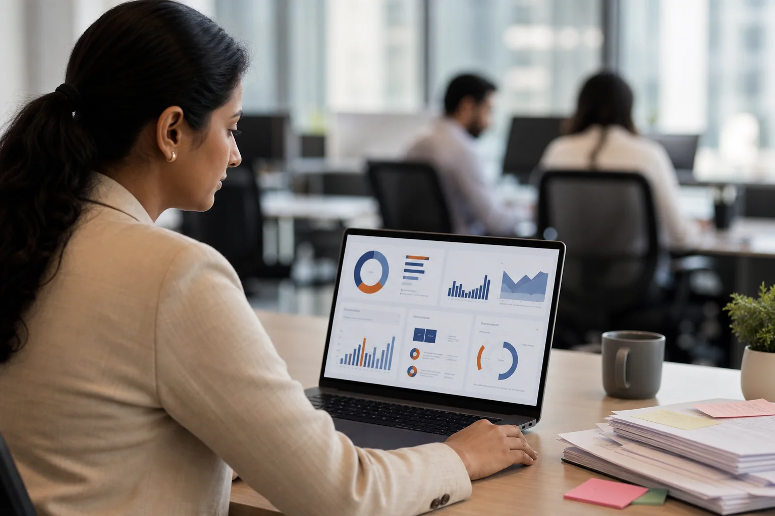 Photorealistic photograph of a focused HR professional at a desk in an Indian corporate office, looking at a laptop screen displaying a clean unified dashboard interface with soft glowing charts in muted blue (#3a5498) and rust orange