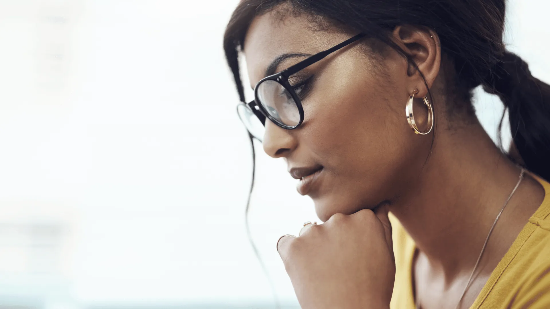 A woman wearing is resting her chin on her hand as she looks at something off screen. She is feeling really good about the instructors and content within the customized learning program developed for her company by Electives.