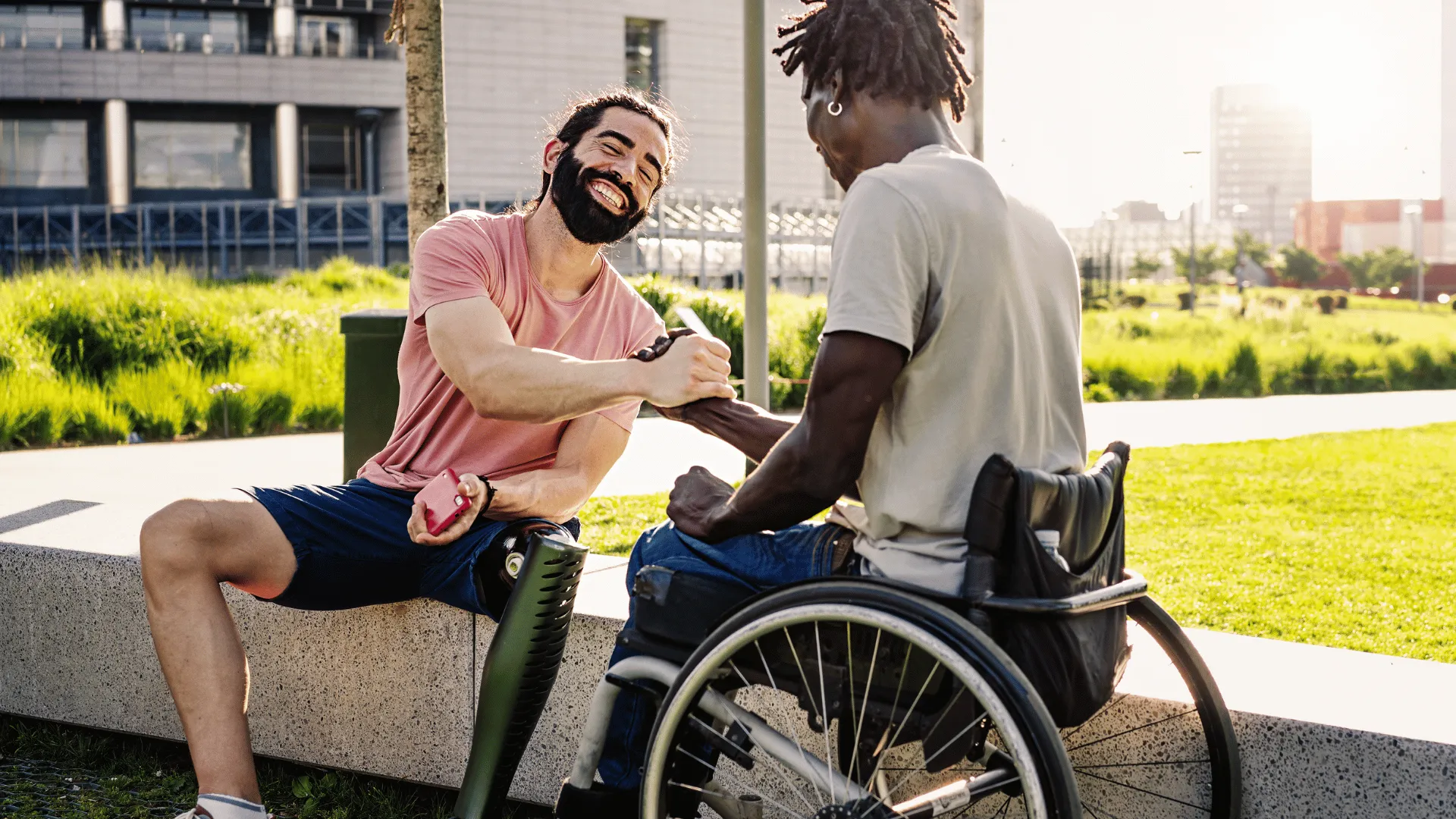 A man with a prosthetic leg and a man in a wheelchair are shaking hands.