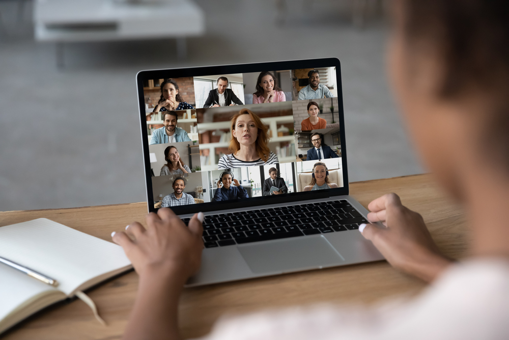 A person sitting at a desk and participating in a Zoom call. We're looking over the person's shoulder.