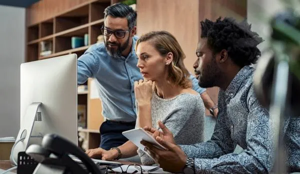 A diverse group of people are working together, looking at a computer monitor.