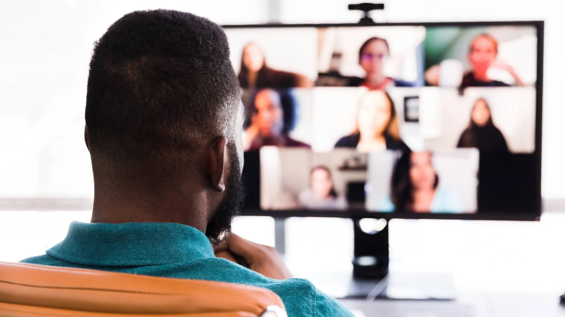 We are looking over a man's shoulder at his computer monitor where he is participating in a virtual live learning session.