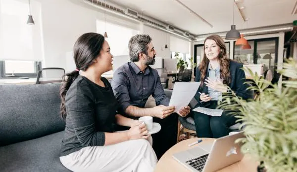 Two women and a man sit in a common space in an office discussing career development.