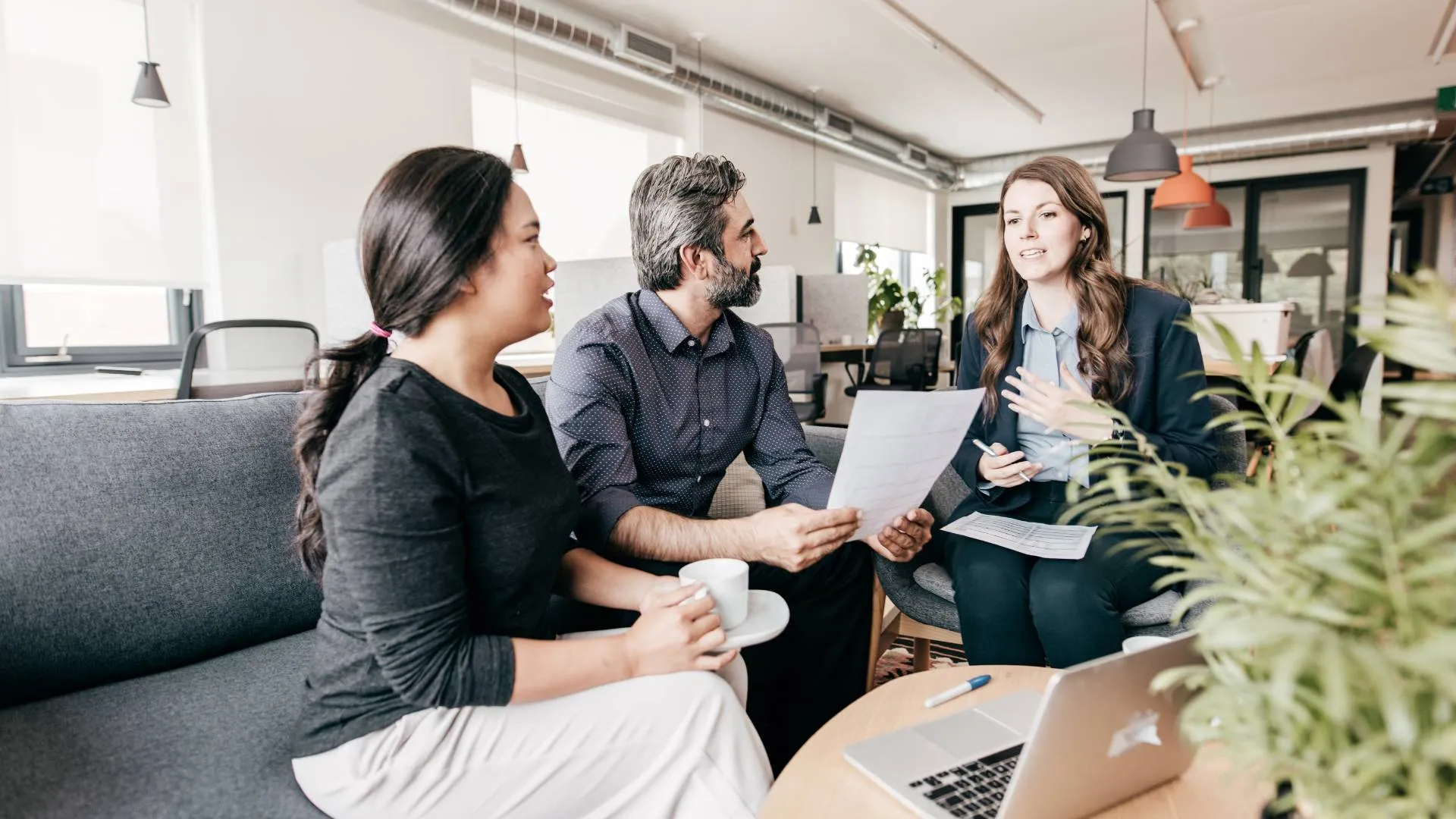 Two women and a man sit in a common space in an office discussing career development.