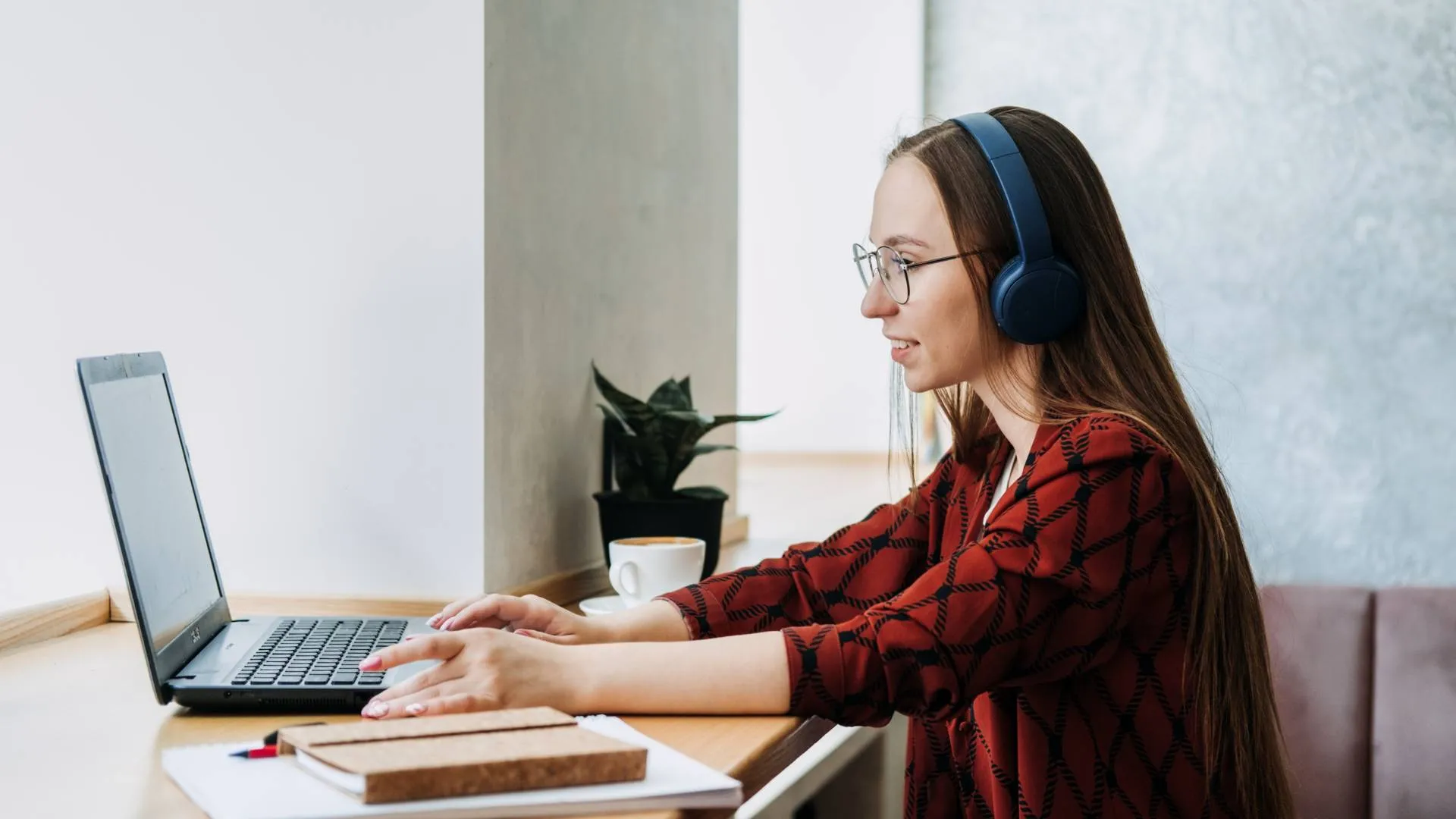A young professional woman sits at a counter working on her laptop wearing headphones.