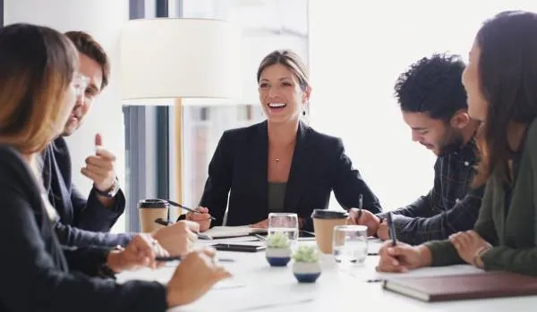 A diverse group of professionals are talking and laughing around a conference table.