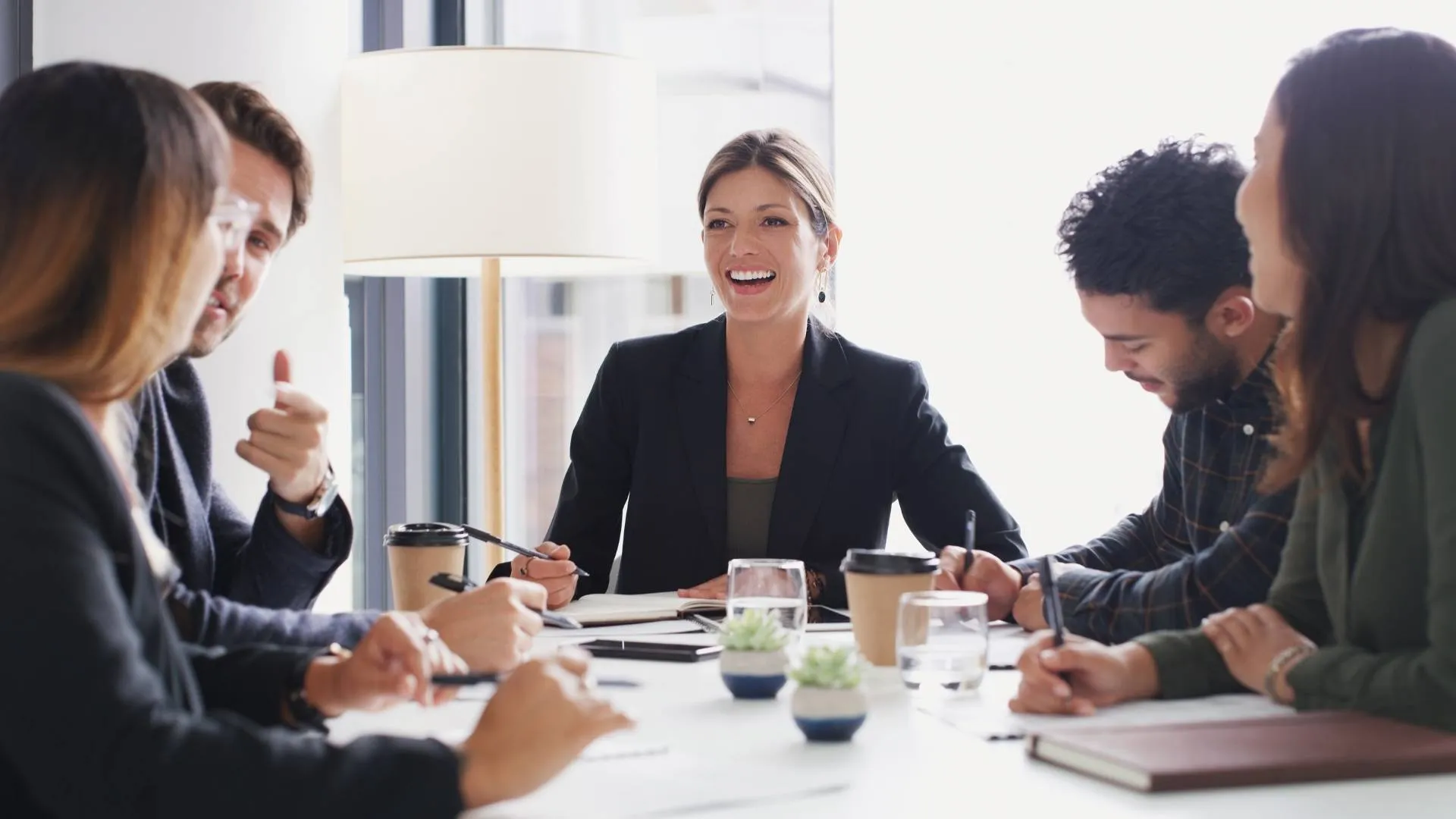 A diverse group of professionals are talking and laughing around a conference table.