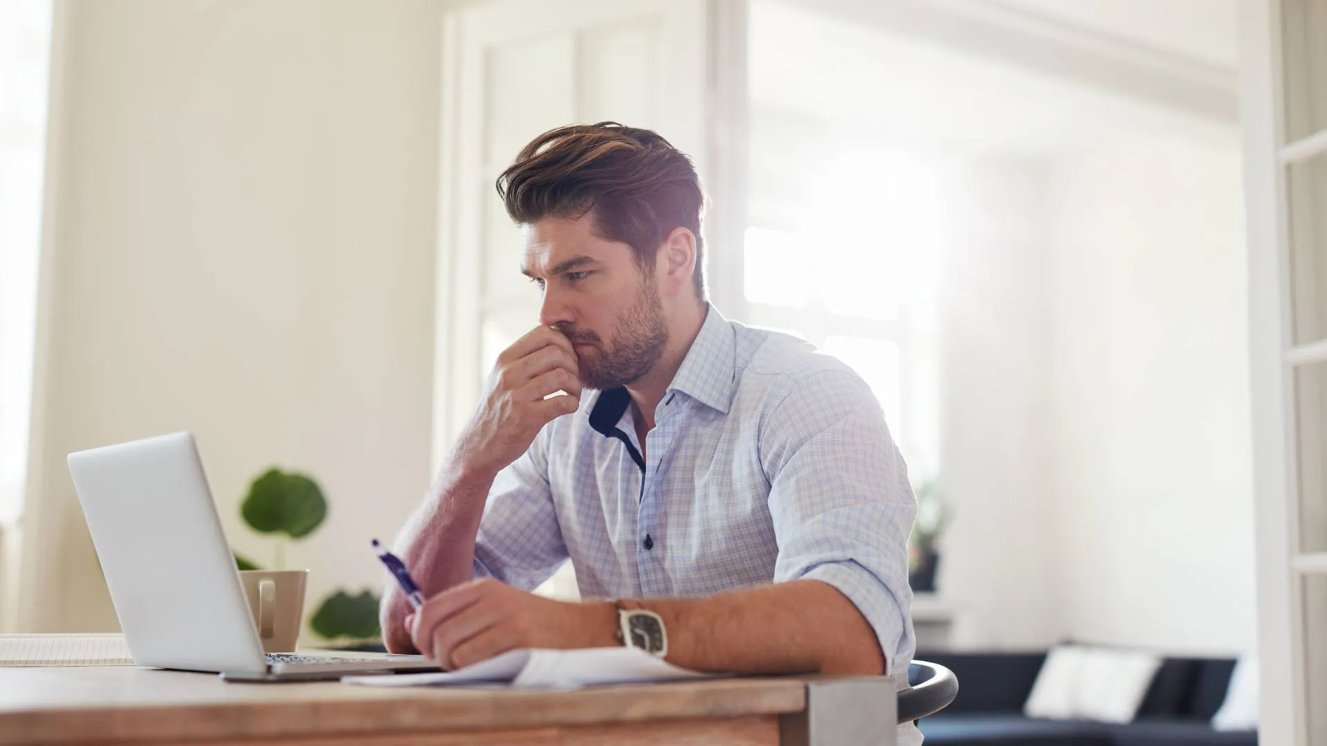 A man is working from home and looking at his laptop with a concerned look on his face.