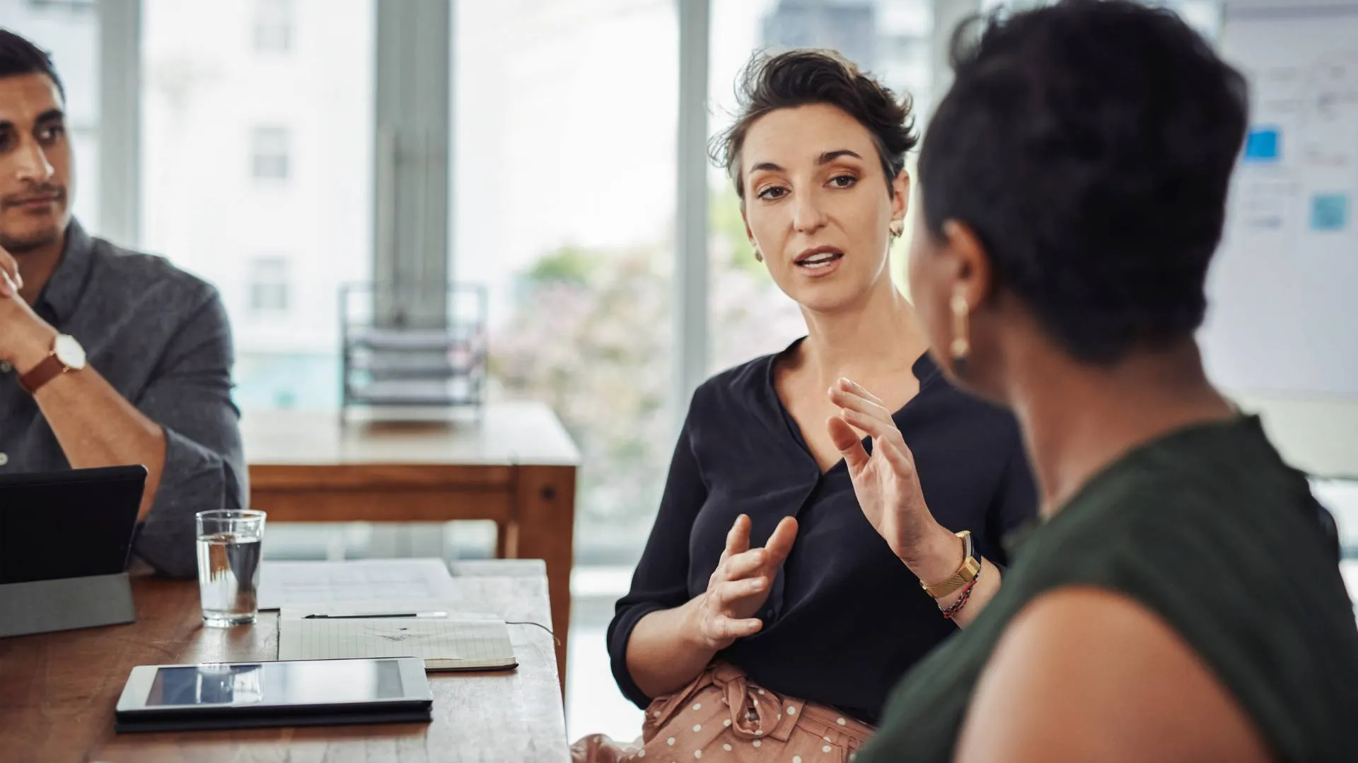 A woman is sitting at a conference table leading a communications training with her colleagues.