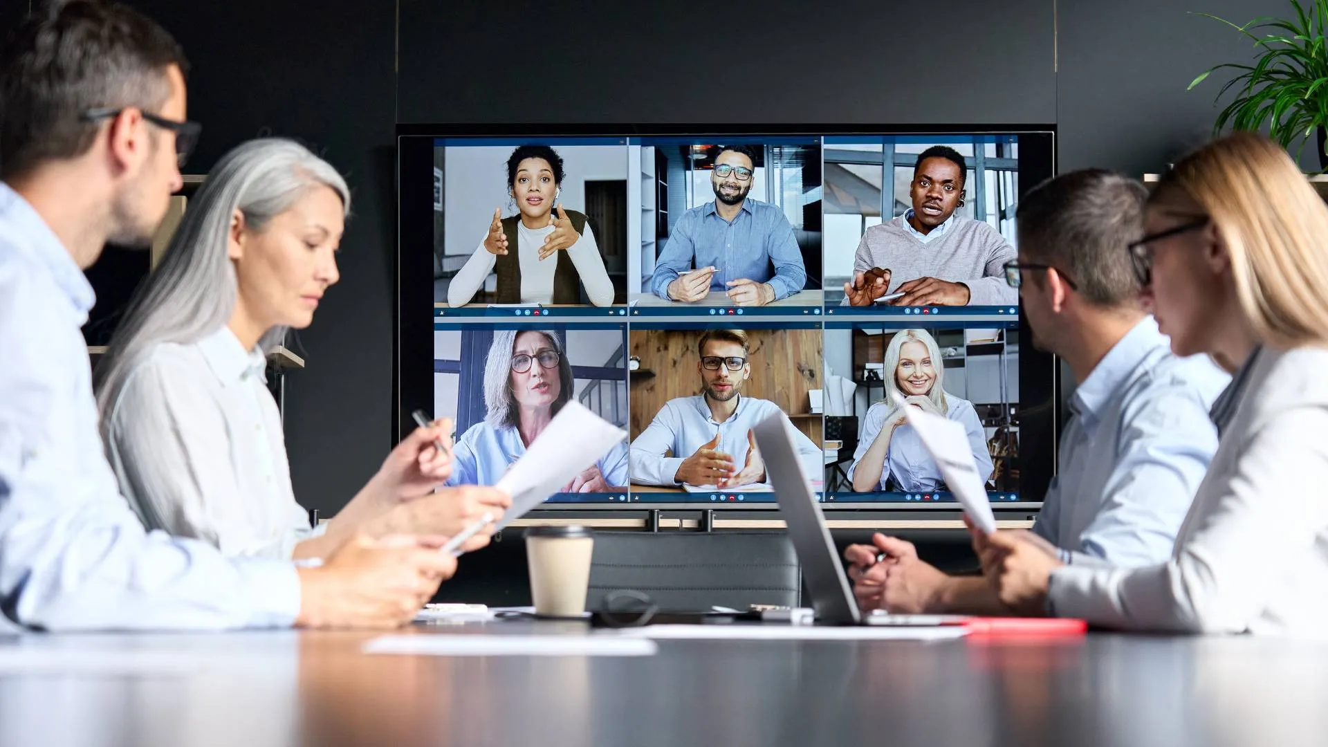 A hybrid team participates in a leadership training. Four are seated at a conference table while 6 are on the screen participating virtually.