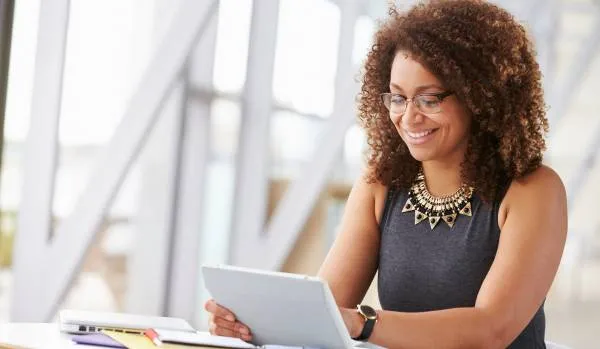 A woman is smiling down at her tablet in her office.