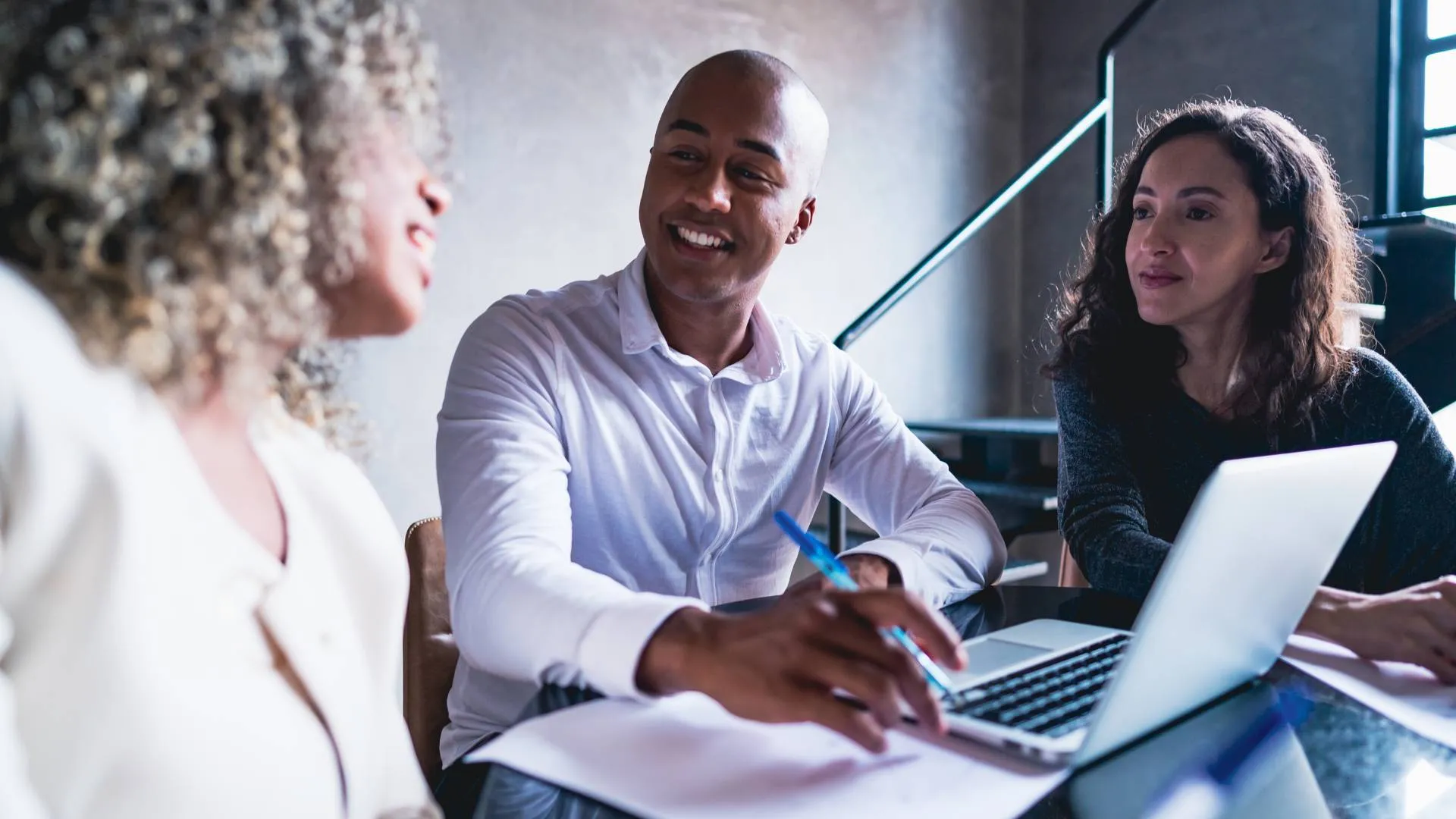 Three professionals are smiling and working together around a laptop.