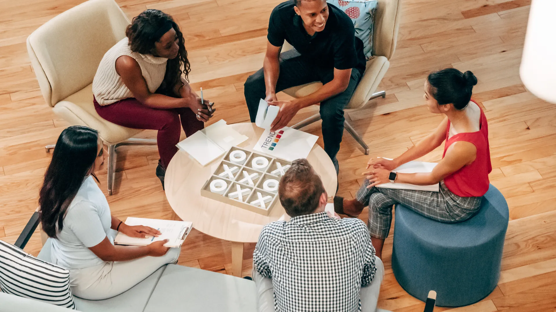 A diverse team of 5 people are sitting in a circle in a common area around a coffee table.