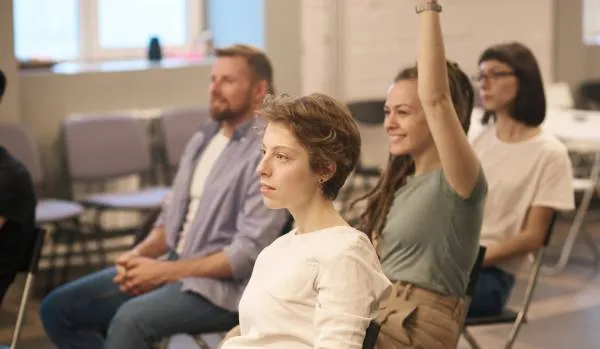 There are four employees sitting in a classroom setting in a training. One woman has her hand raised.