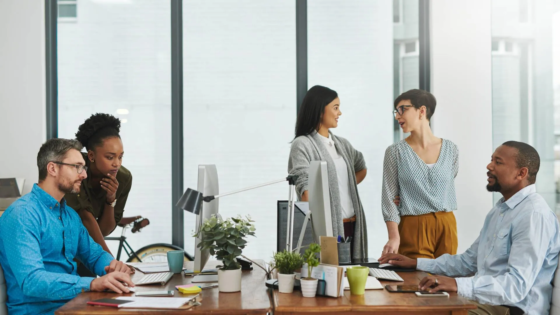 There are five employees in a conference room having a meeting at table.