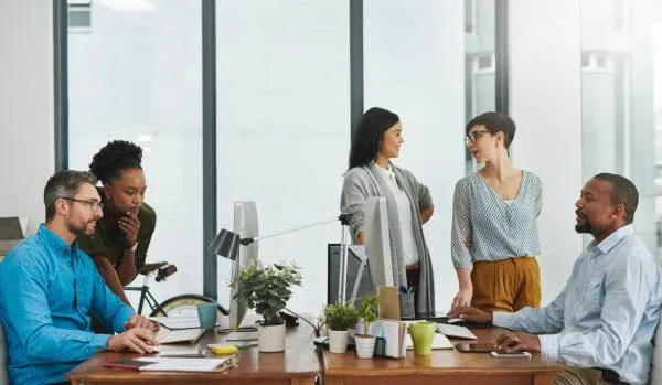 There are five employees in a conference room having a meeting at table.