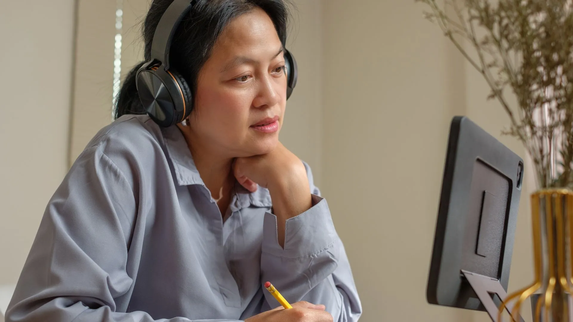 A woman with headphones looks at her computer monitor. She is participating in employee training.