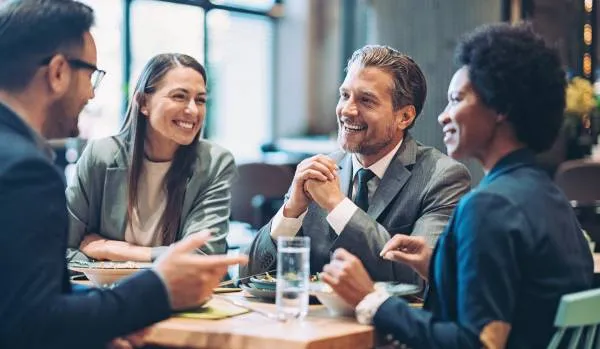 A group of colleagues are talking and laughing over lunch in a restaurant.