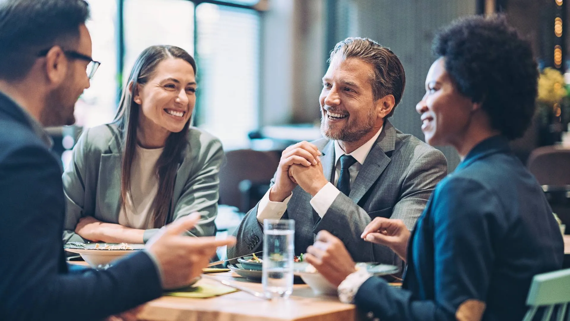 A group of colleagues are talking and laughing over lunch in a restaurant.