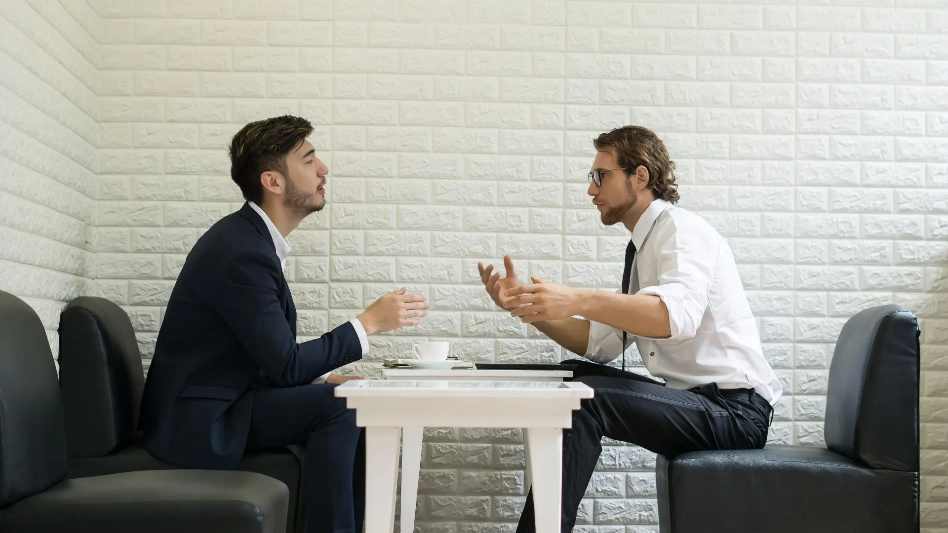 Two men sit across from a table talking during a one-on-one meeting. The manager is sitting on the left and is glad he was trained to handle emotional employees before coming to this meeting.