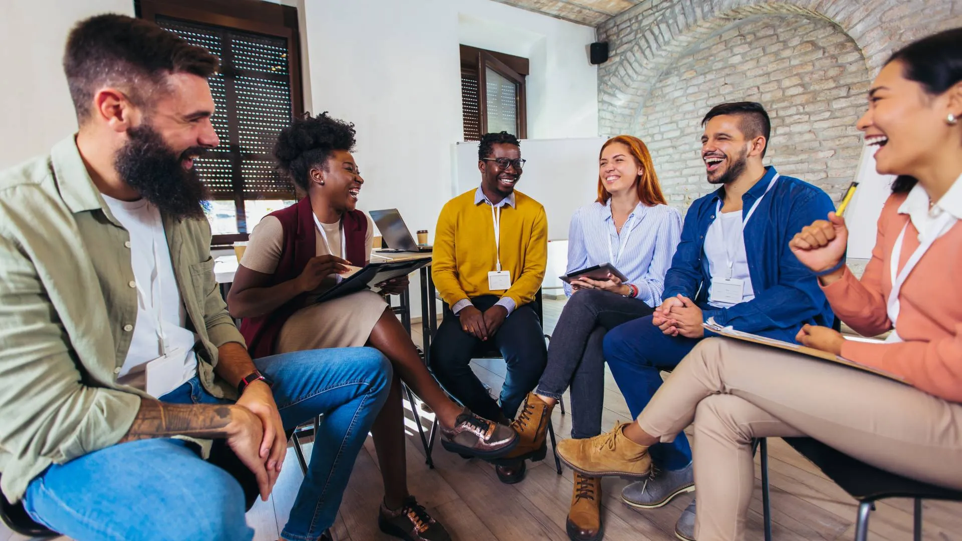 A group of diverse employees are sitting in a circle, laughing and smiling.