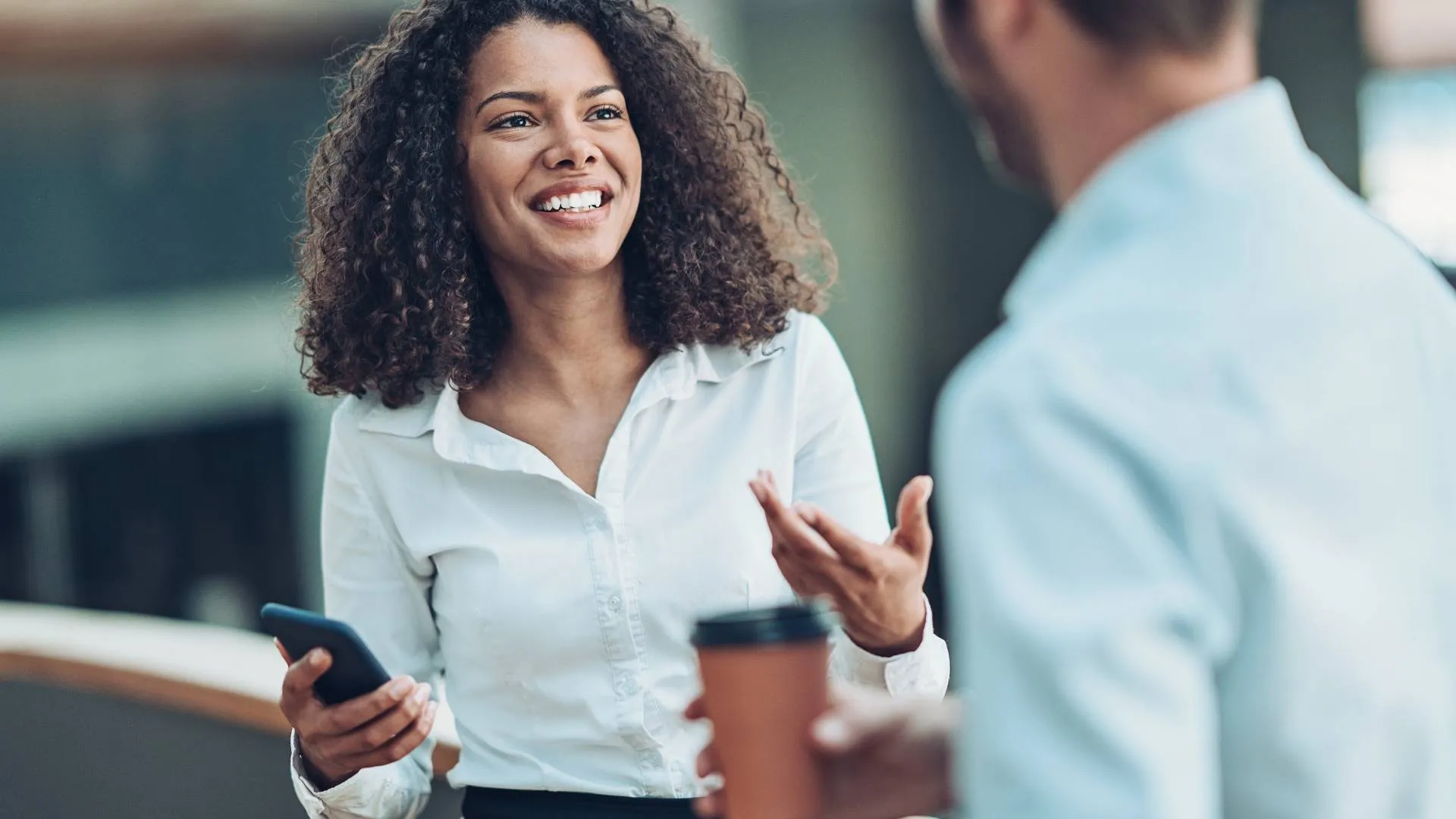 We are looking over a man's shoulder at a smiling woman who is talking to him.